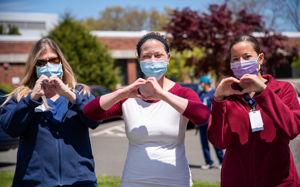 Healthcare workers showing appreciation wearing protective face masks and forming heart shapes with their hands as a gesture of solidarity and compassion during challenging times.